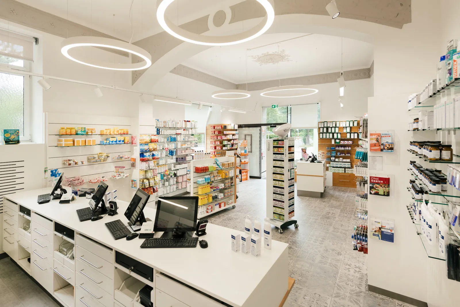Blick durch den Verkaufsraum der Saggen-Apotheke mit Ringleuchten, Regalen und Theke